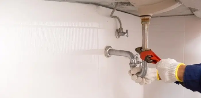 Person repairing a leaking pipe under a bathroom sink