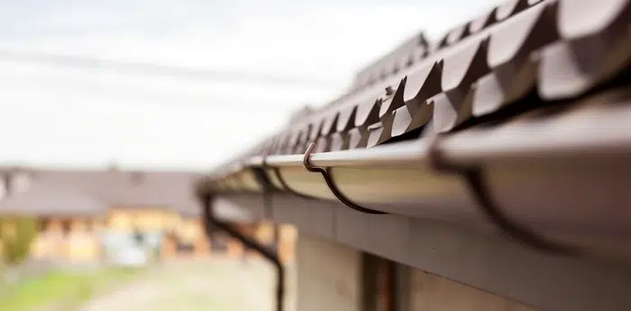 Person on a ladder cleaning leaves out of a house gutter