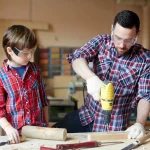 Father and son working on a woodworking project together indoors, focused and dressed casually